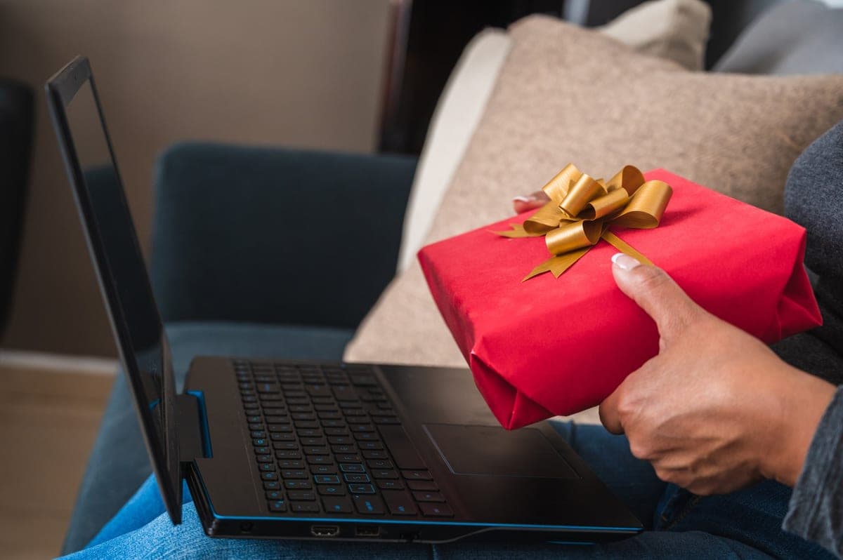 Mujer sonriendo con una caja de regalo roja frente a su portátil, simbolizando las recomendaciones de regalo generadas por IA